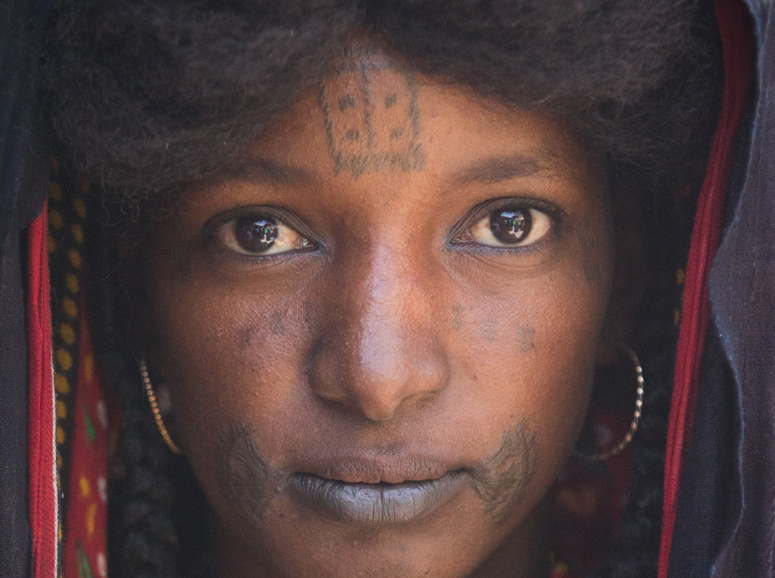 A young Wodaabe girl has facial tattooes and a hairstyle that is common.