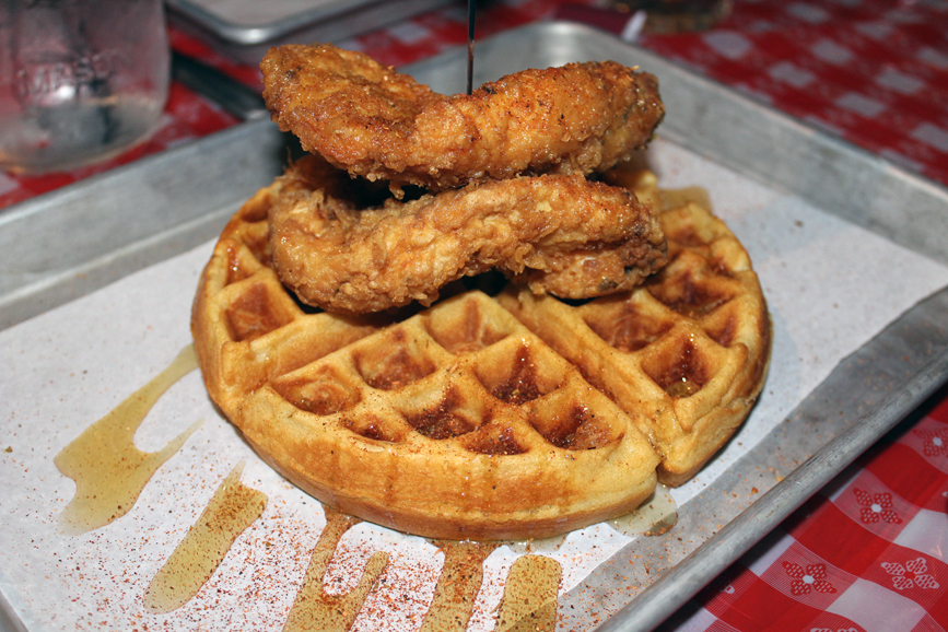 A crispy golden waffle topped with a fried boneless chicken breast and lightly sprinkled with honey and ground pepper. Photograph by Aleesia Forni.