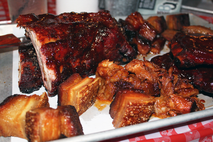 A sampling of smoked meats, including a half rack of Memphis dry rub ribs, a half rack of St. Louis sticky ribs, beer ribs, kielbasa, smoked turkey, smoked chicken, pulled pork, pork belly, burnt ends and beef brisket, topped with house-made barbecue sauce. Photograph by Aleesia Forni.