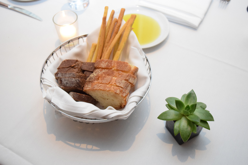 A basket of assorted breads and breadsticks is served alongside a bowl of olive oil. Photograph by Aleesia Forni.