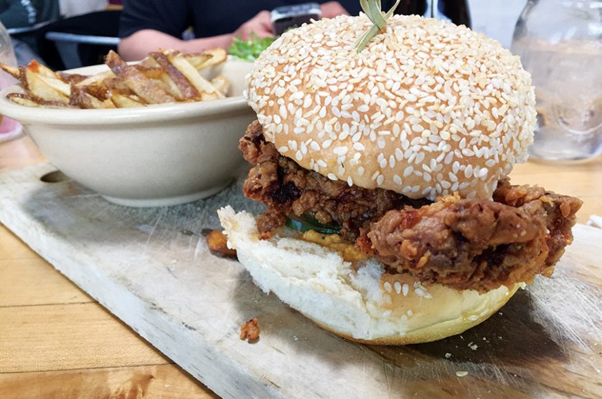 A fried chicken sandwich artfully presented on a wooden slab. Photograph by Aleesia Forni.