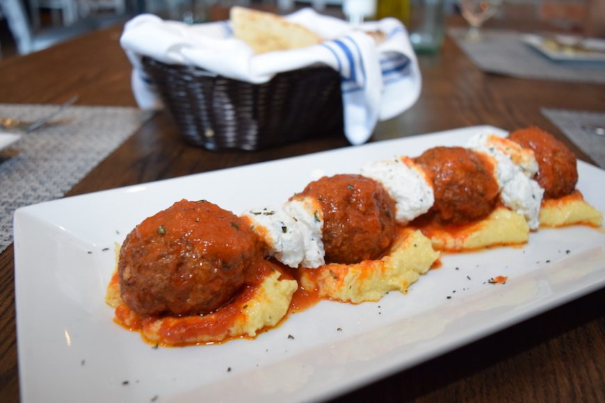 Meatballs are piled above a helping of polenta, topped with fresh herbs and ricotta cheese. 