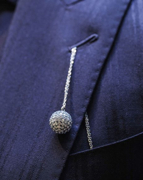 The pavé-set diamond Mirror Ball pendant in blackened 18-carat white gold, worn in the lapel of a Sir Tom Baker city suit.