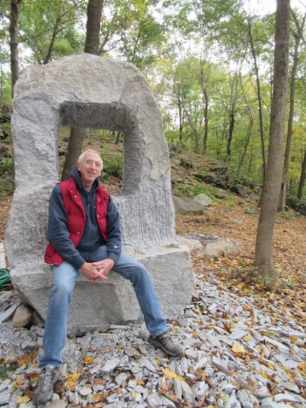 Stone sculptor Bob Madden with his finished work, “Window to the Past,” at Crystal Park in Holmes. Photograph by Mary Shustack.