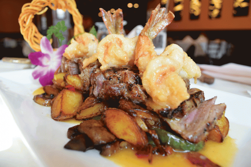 A 10-ounce steak sits on a bed of potatoes and is topped with shrimp.
