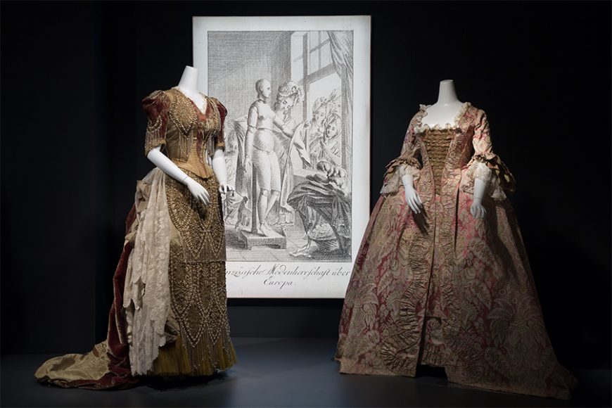 From left: Emile Pasquier, green and brown changeant velvet and green faille ball gown, 1889-1890, France. The Museum at FIT; “Französische Modenherrschaft über Europa” (French Fashion Domination over Europe). Etching by Christian Gottlieb Geyser after Daniel Nikolaus Chodowiecki, circa 1780, Germanisches Nationalmuseum, Nuremberg, HB 25963, Kapsel 1267. ©Germanisches Nationalmusuem, photograph: Monika Runge. Light box and graphic imagery provided by Leach, a subsidiary of Chargeurs; and Pink and green lace patterned silk robe à la française, 1750s, probably France. The Museum at FIT. ©The Museum at FIT.