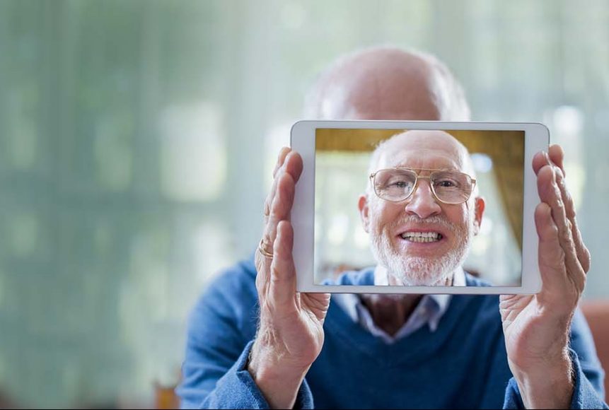 Portrait of happy senior man taking self portrait through digital tablet in nursing home