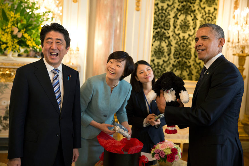 President Barack Obama holds up a golf club cover resembling first pooch Bo, a Portuguese Water Dog, a gift of then Japanese Prime Minister Shinzō Abe and first lady Akie Abe (pictured here), presented at Akasaka Palace in Tokyo on  April 24, 2014. Photograph by Pete Souza for the White House.